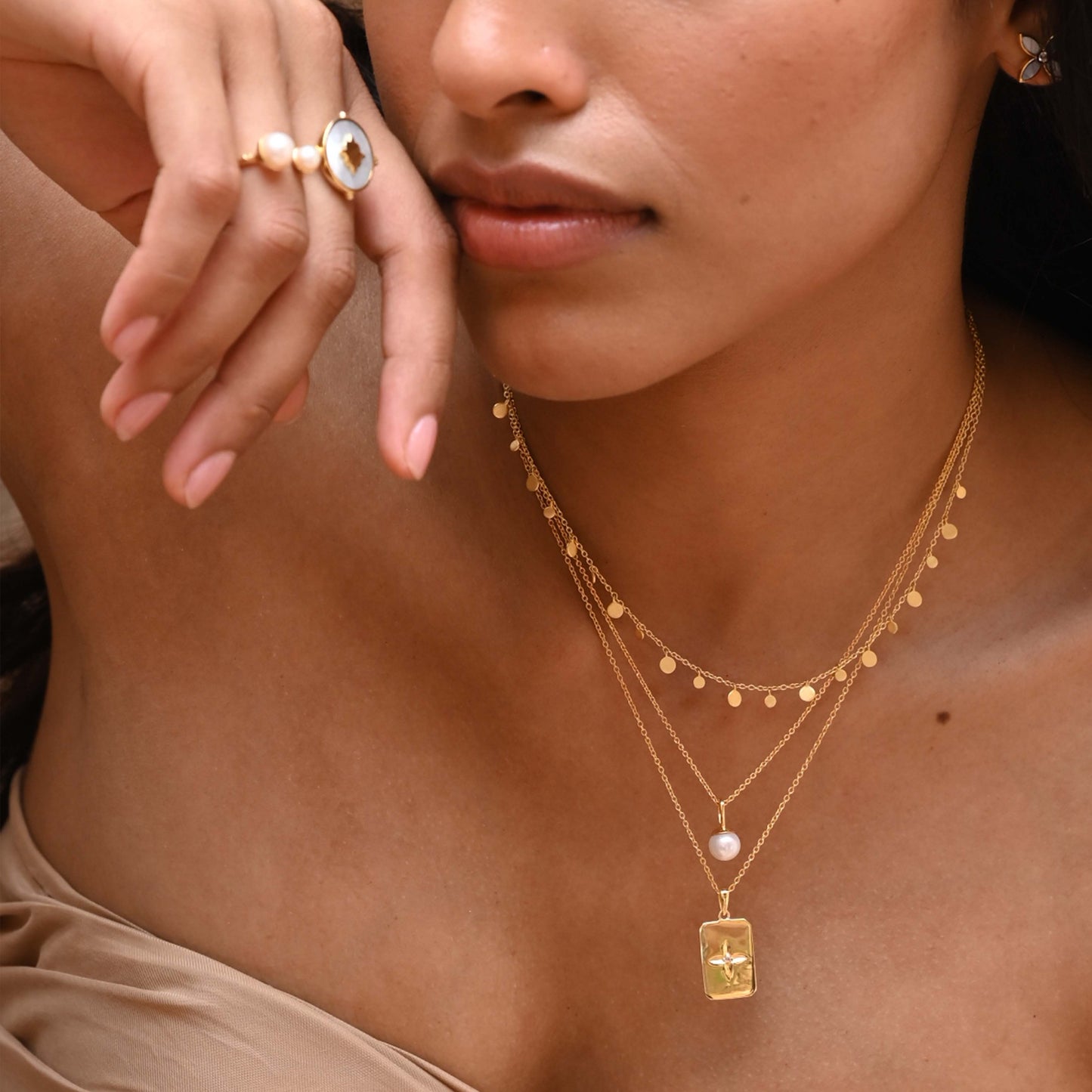 Close-up of a woman wearing gold jewelry including a necklace, ring, and earrings.