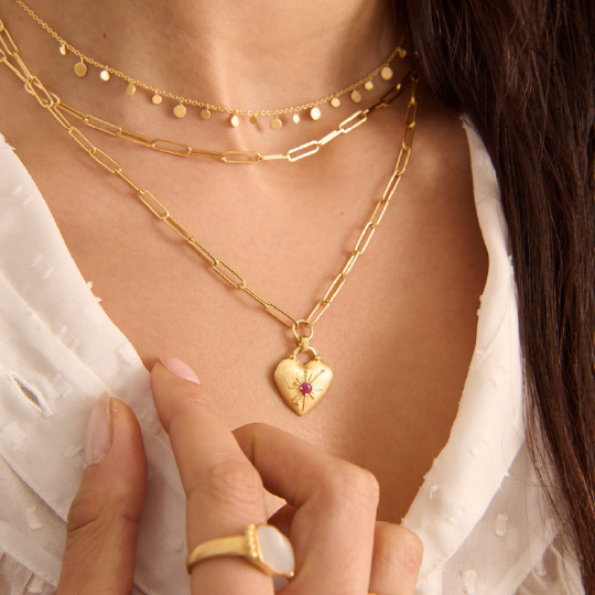 Close-up of a person wearing gold necklaces with a heart-shaped pendant.