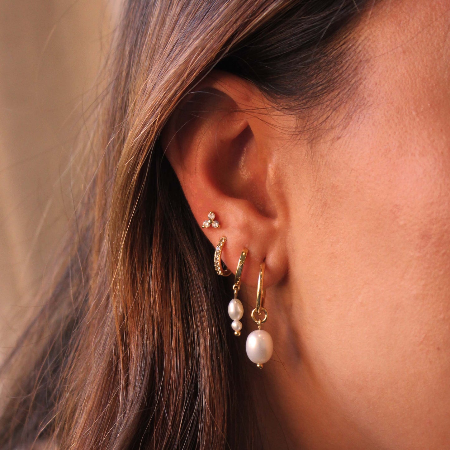 Close-up of an ear with multiple gold and pearl earrings against a neutral background
