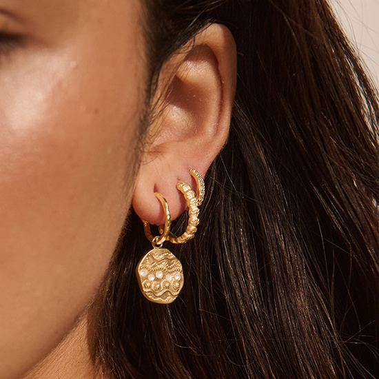 Close-up of a person wearing gold hoop earrings with dangling elements.