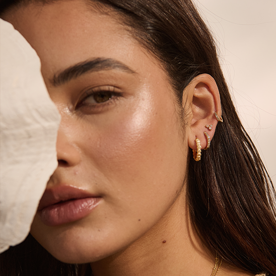 Close-up of a woman wearing gold hoop earrings with a neutral background