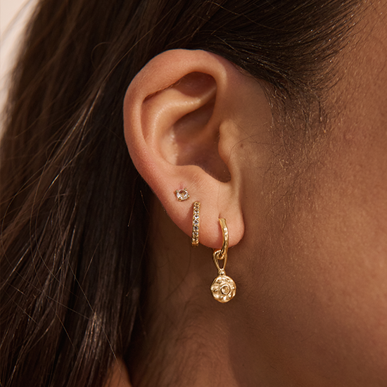 Close-up of an ear wearing gold hoop earrings with a small round earring.