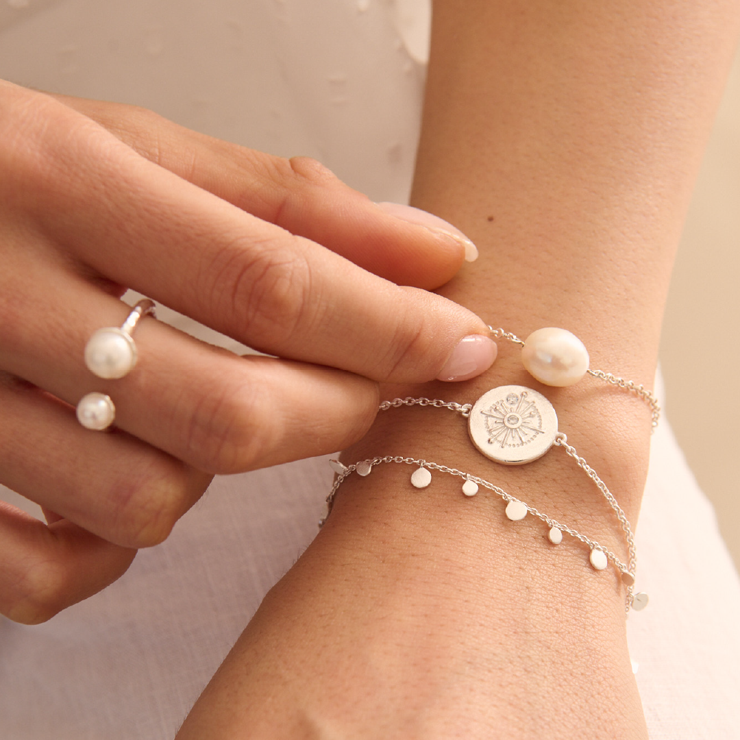 Close-up of a hand wearing pearl rings and a silver bracelet with a circular charm.
