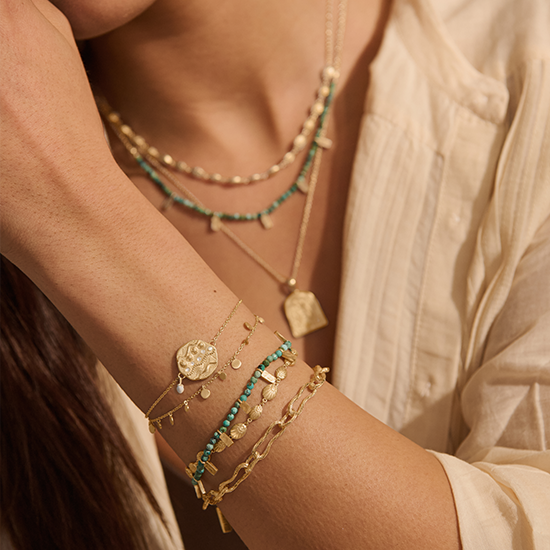 Close-up of a person wearing multiple gold and green beaded bracelets on their wrist.