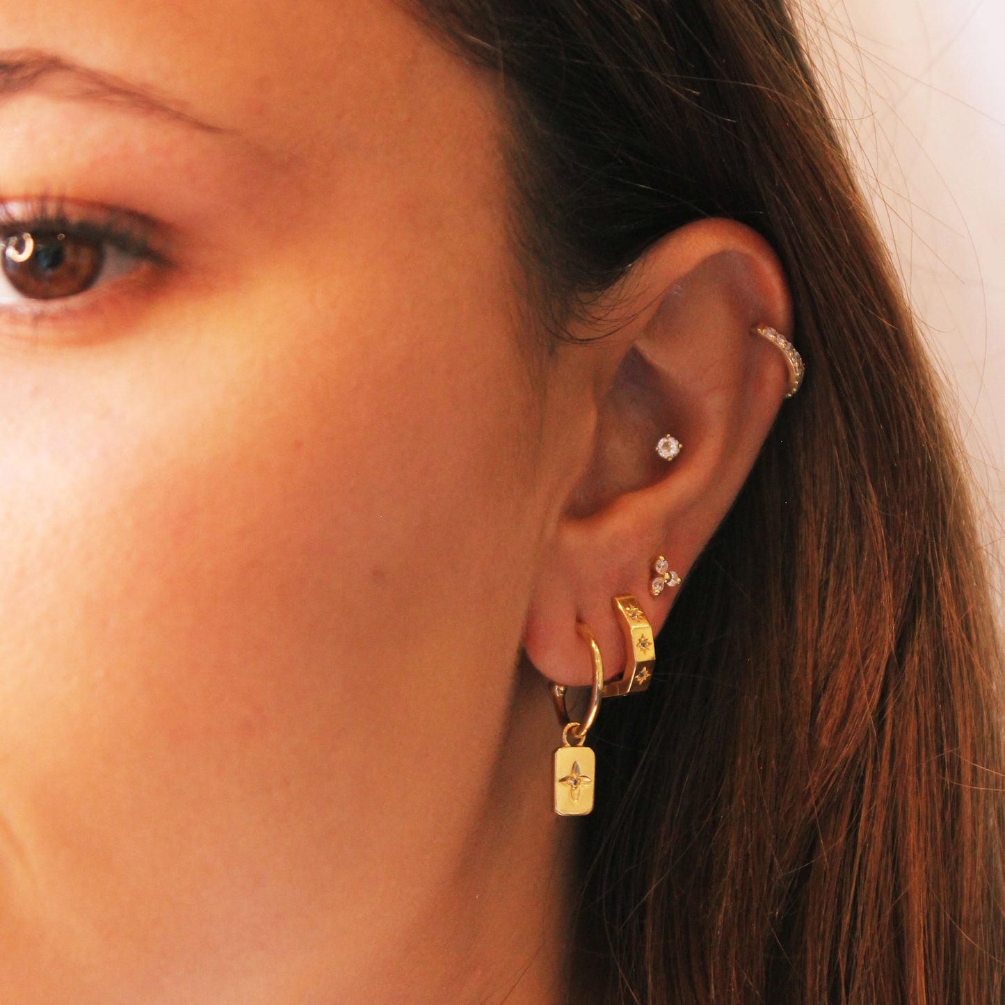 Close-up of a person's ear with multiple earrings on a neutral background