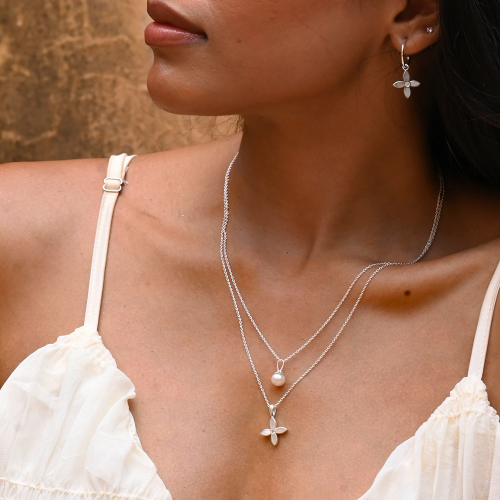 Woman wearing a silver necklace with a pendant and matching earrings against a neutral background