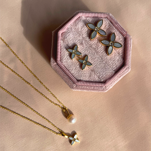 Flower-shaped earrings on a pink hexagonal jewelry dish with a gold necklace on a beige background