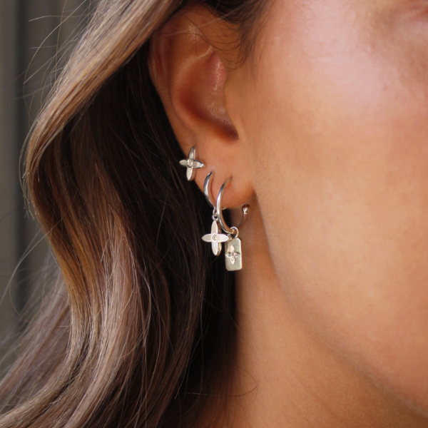 Close-up of an ear wearing silver hoop earrings with star-shaped charms.