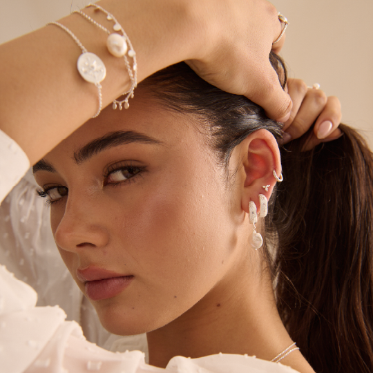 Close-up of a woman wearing pearl earrings and jewelry, with a neutral background.