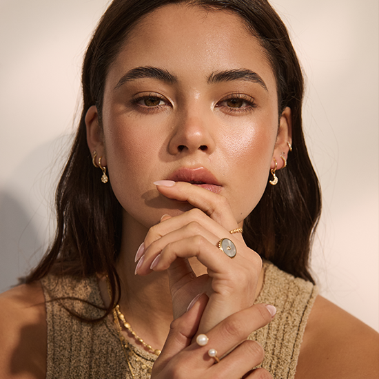 Woman with jewelry including earrings, a necklace, and rings on a neutral background