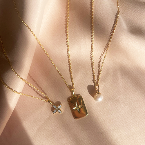Three gold necklaces with different pendants on a soft pink background