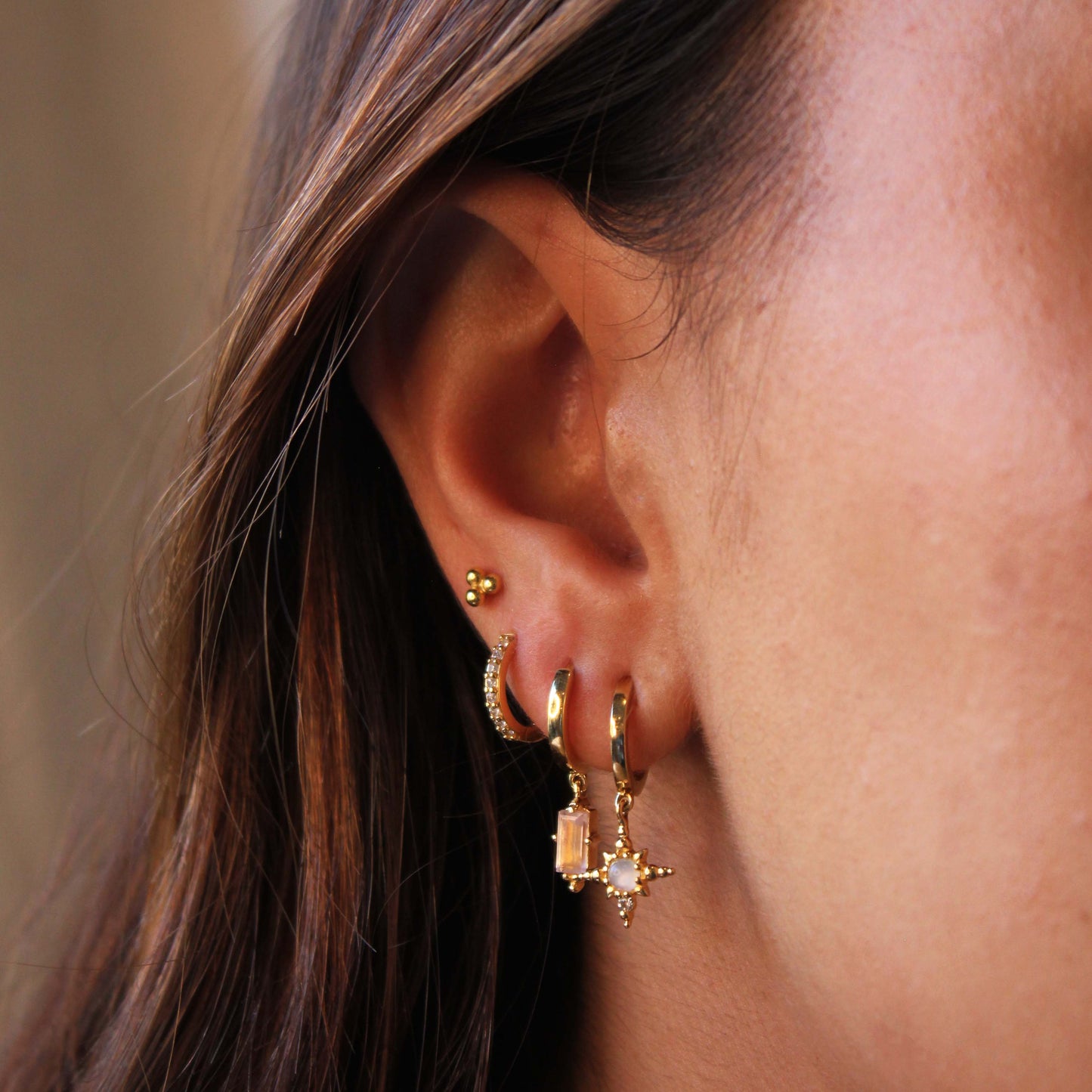 Close-up of an ear wearing gold hoop earrings with a blurred background