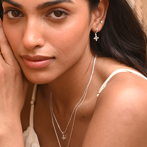 Close-up of a woman wearing silver earrings and necklaces against a neutral background