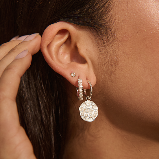Close-up of an ear wearing silver earrings with a hand adjusting hair.