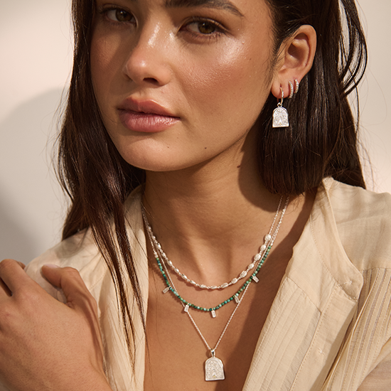 Woman wearing layered necklaces and earrings with a neutral background