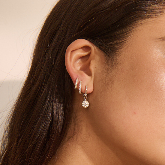 Close-up of an ear with multiple earrings against a neutral background