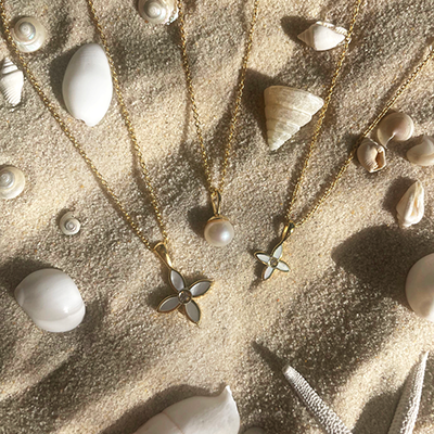 Gold necklaces with pearl pendants on a sandy surface with seashells.