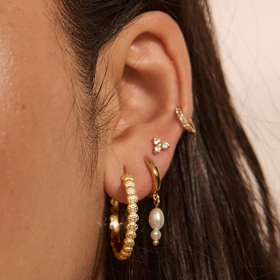 Close-up of an ear with gold and pearl earrings on a neutral background