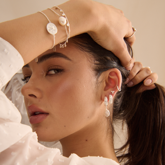 Close-up of a woman wearing pearl earrings and bracelets against a neutral background