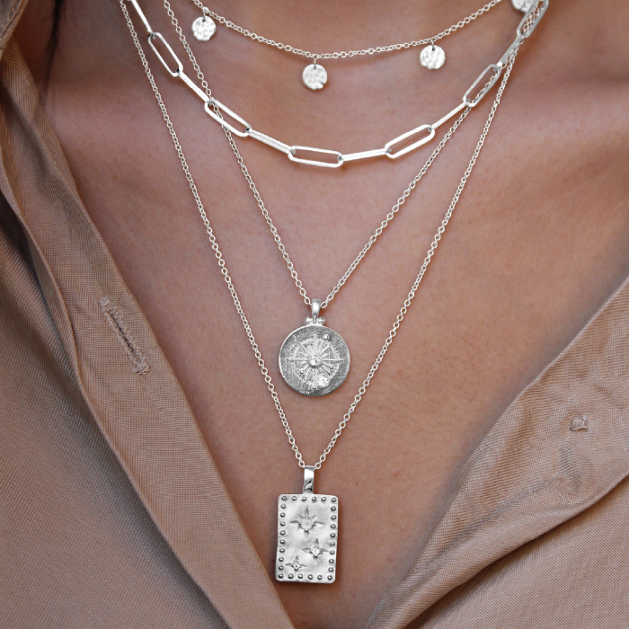 Layered silver necklaces with pendants on a person wearing a beige top.