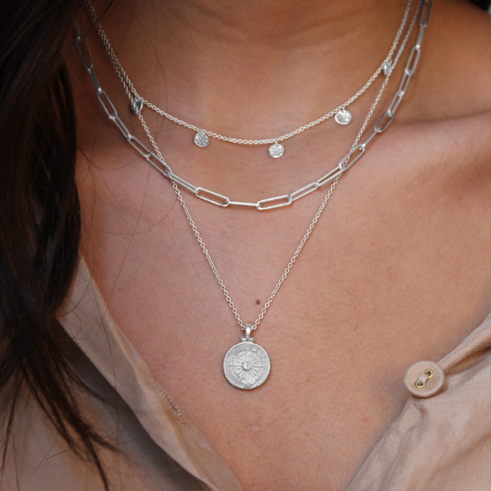 Close-up of layered silver necklaces on a person wearing a sheer beige top.