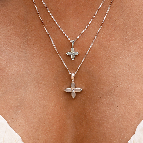 Two silver flower-shaped necklaces on a person's neck against a neutral background