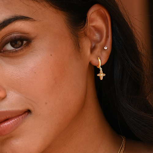 Close-up of a woman's ear wearing gold earrings with a blurred background