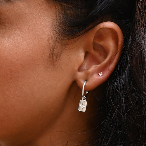 Close-up of an ear wearing a silver earring with a tag detail.