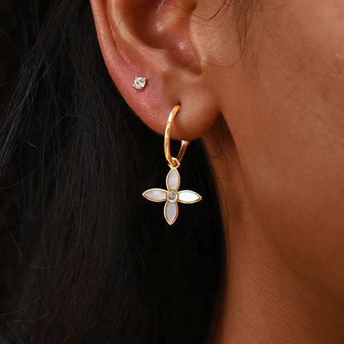 Close-up of an ear wearing a gold hoop earring with a floral pendant.