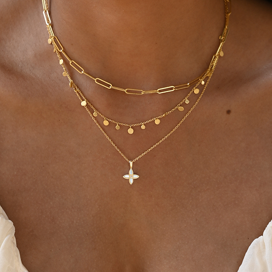 Gold necklaces with a star pendant on a person's neck against a neutral background