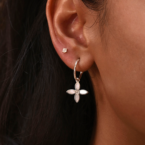 Close-up of an ear wearing a silver hoop earring with a floral design.