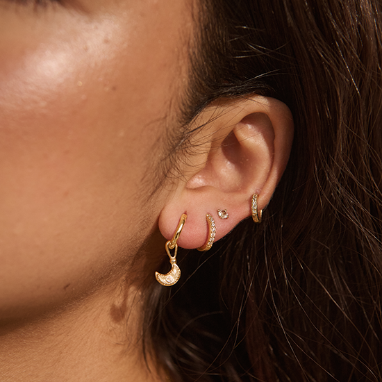 Close-up of an ear wearing gold hoop earrings with a blurred background