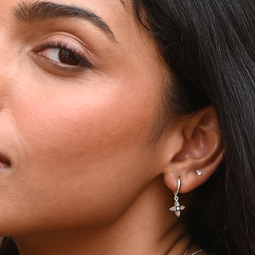 Close-up of a woman's ear wearing silver earrings with a neutral background