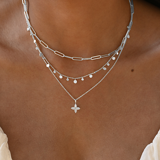 Layered silver necklaces on a person's neck with a neutral background